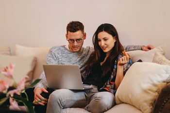 Couple on couch viewing an open laptop together.